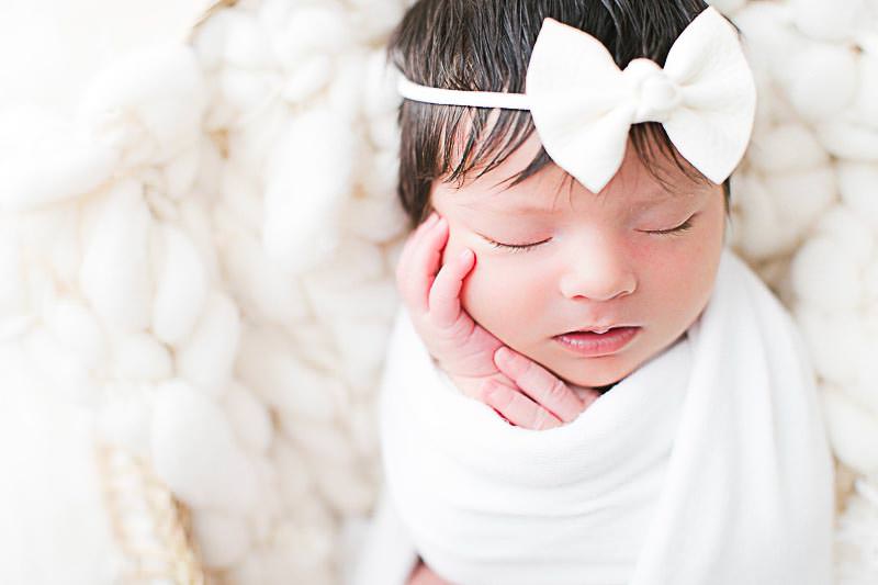 Photographie de naissance d'une petite fille de quelques jours avec un nœud blanc